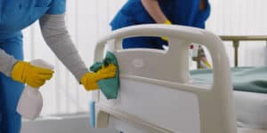 Two hospital cleaning janitors in their uniforms using cleaning equipment to clean the hospital bed in the ward
