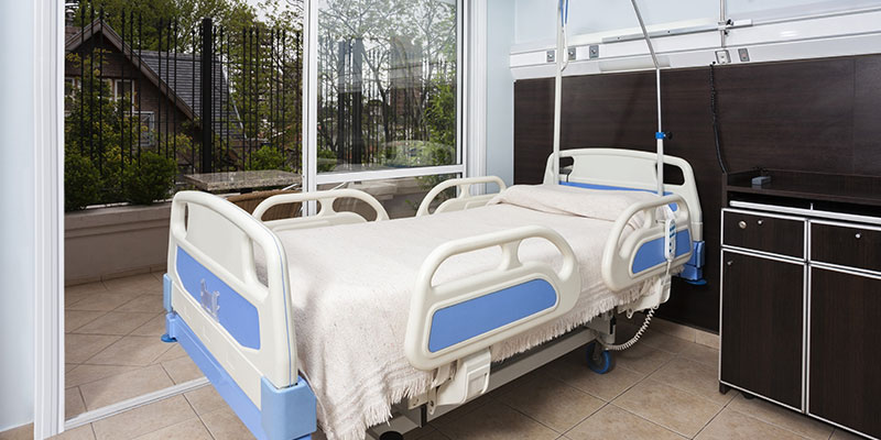 Interior view of a hospital that is seen with bed, Air Conditioner, cub board and other medical equipment.