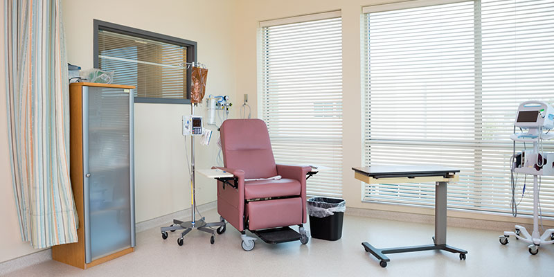 A hospital room that has empty chair, IV drip stand, table, cub board and all other things needed for chemo therapy.